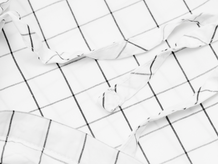 Nærbillede af en hvid skjorte med sort gittermønster, med en knap og noget krøllet stof.