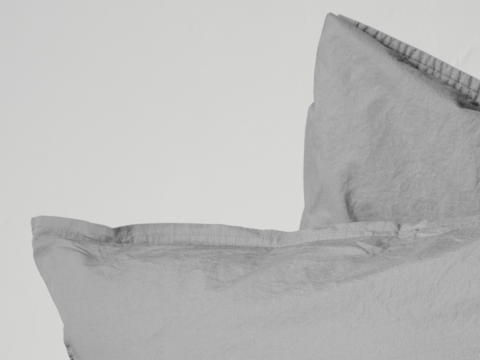 To lysegrå puder med synlige sømme stablet mod en hvid baggrund.