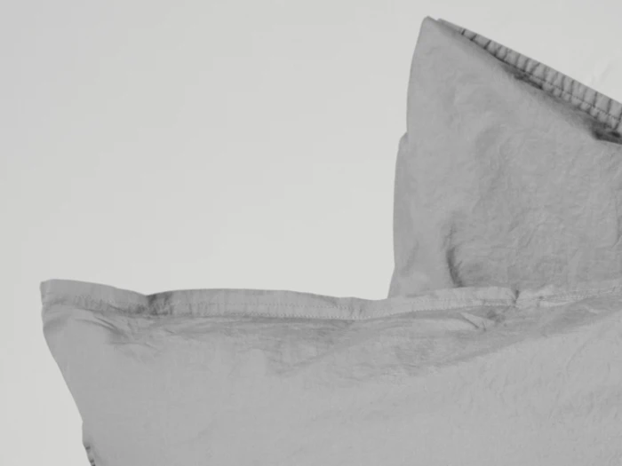 To lysegrå puder med synlige sømme stablet mod en hvid baggrund.