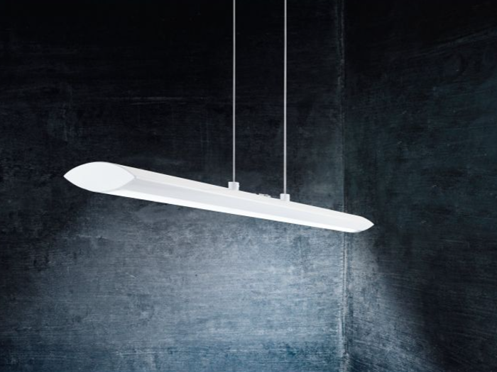 En moderne hvid pendel hænger fra loftet i to kabler mod en mørk, struktureret væg.