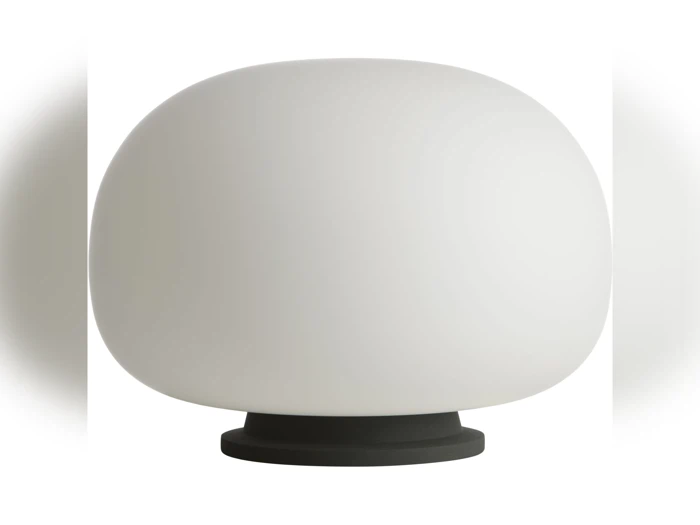En moderne bordlampe med en stor, afrundet hvid lampeskærm og en lille, cirkulær sort fod på en ensfarvet hvid baggrund.