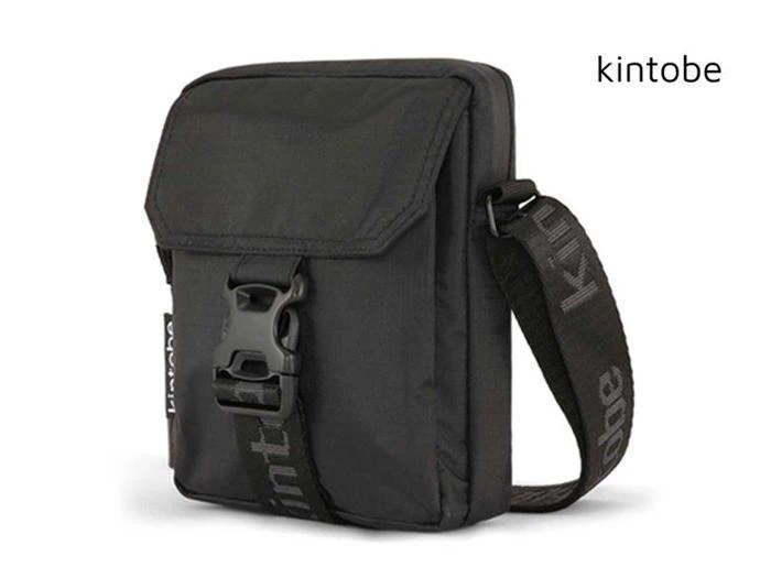 En lille sort crossbody-taske med spænde foran, flaplukning og en justerbar rem, hvor der står kintobe på. Mærkets navn står også i øverste højre hjørne.
