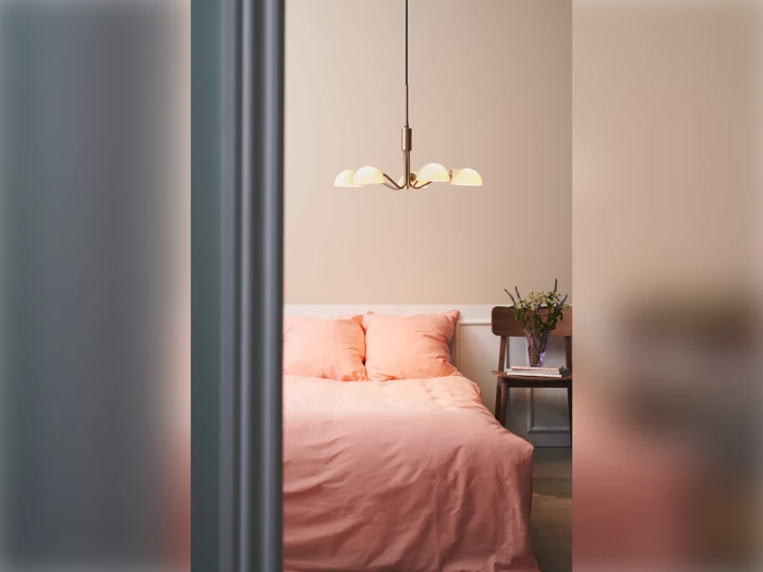 Et hyggeligt soveværelse med en dobbeltseng dækket af blødt rosa sengetøj, en moderne pendel over sengen og et natbord med en vase med blomster.