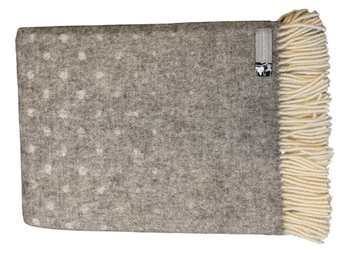 Et foldet gråt uldtæppe med et diskret prikket mønster og cremefarvede frynser i den ene ende, med et mærke i øverste højre hjørne.