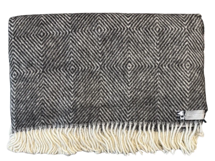 Et foldet sort og hvidt geometrisk mønstret uldtæppe med cremefarvede frynser langs kanten og en lille etiket i hjørnet.