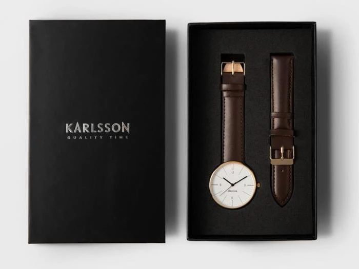 En sort Karlsson-urkasse med et armbåndsur med guldkant og en ekstra brun læderrem udstillet side om side.