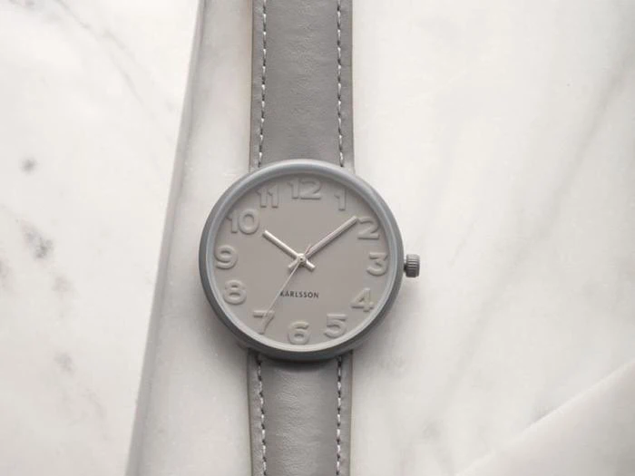 Et minimalistisk gråt armbåndsur med store tal på et matchende gråt bånd, placeret på en lys marmoroverflade.