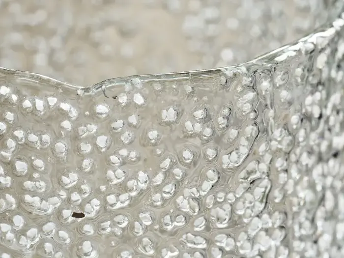 Nærbillede af en struktureret, klar glasoverflade med en bølget, ujævn kant og hævede boblelignende mønstre.