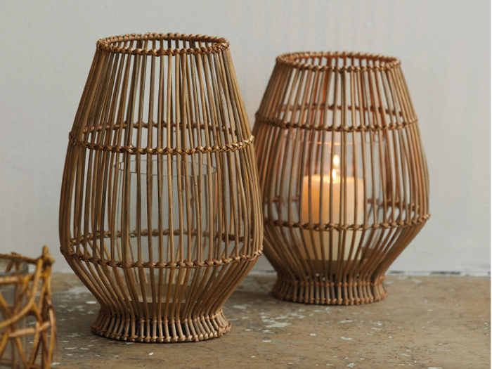 To flettede lanterner, den ene med et tændt hvidt lys, er placeret på en plettet bordplade mod en ensfarvet lys væg.