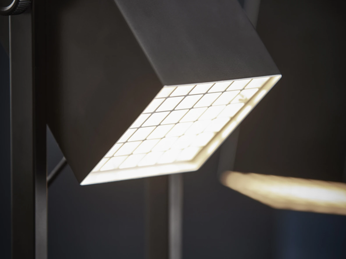 Et nærbillede af en moderne, firkantet lampe med en diffusor med gittermønster, der udsender klart hvidt lys.