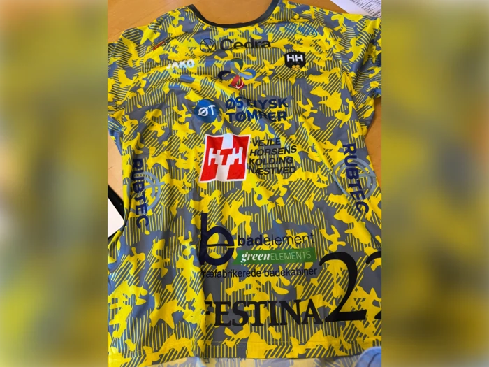 Gul og grå sportstrøje med forskellige sponsorlogoer og tekst, herunder HESTINA, HH og adskillige andre sorte, blå og røde logoer på forsiden.