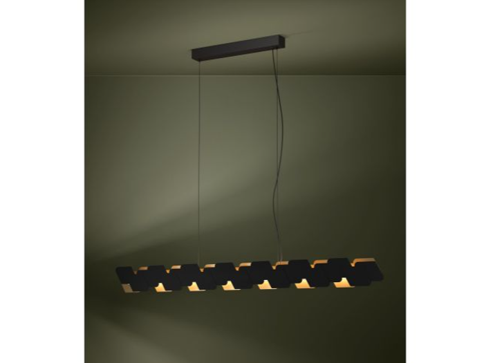 Moderne sort pendel med geometriske, sammenkoblede former, der hænger fra loftet mod en olivengrøn væg og blødt oplyser rummet nedenunder.