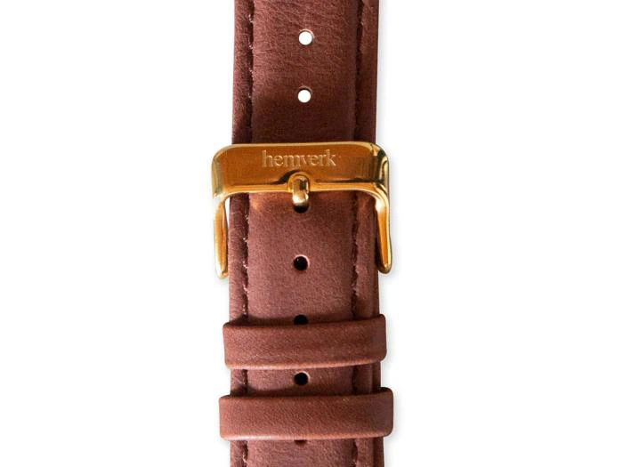 Nærbillede af en brun læderurrem med et guldspænde med ordet hemverk indgraveret.