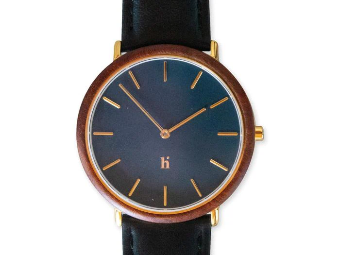 Et minimalistisk armbåndsur med en mørk urskive, timemarkeringer og visere i guld, en træramme og en sort læderrem.