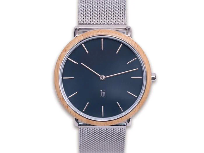 Et minimalistisk armbåndsur med sort urskive, sølvfarvede timemarkeringer, en lys træramme og en sølvfarvet netrem på en hvid baggrund.