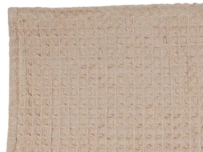 Nærbillede af et beige håndklæde med et struktureret, gitterlignende vaffelvævet mønster. Kun en del af håndklædet er vist.
