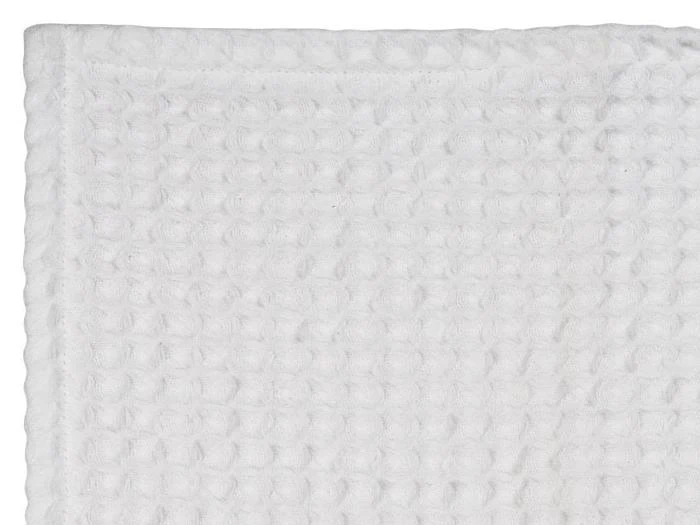 Et nærbillede af et hvidt, struktureret, vaffelmønstret håndklæde eller stof, set fra siden med synlige vævede detaljer.