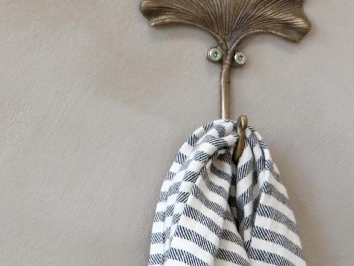 En messingknage formet som et blad holder et sort- og hvidstribet håndklæde op mod en lys væg.