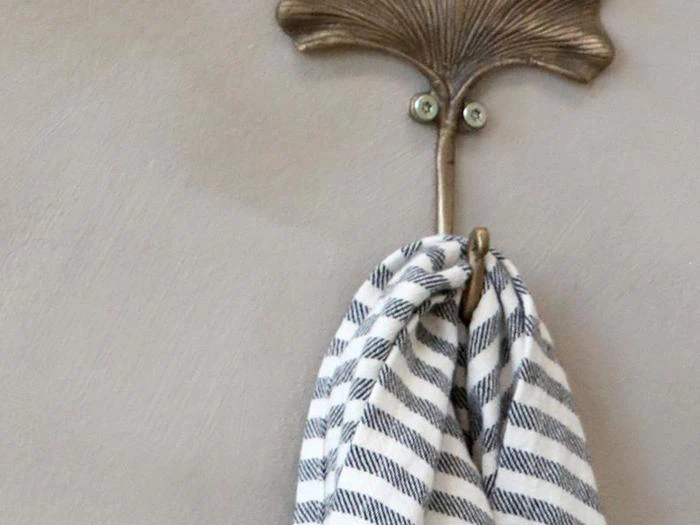 En messingknage formet som et blad holder et sort- og hvidstribet håndklæde op mod en lys væg.