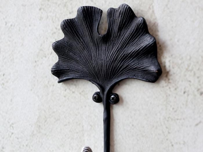 En sort metalknage formet som et ginkgoblad, monteret på en lys væg.