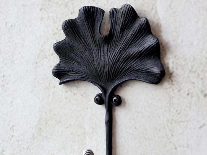 En sort metalknage formet som et ginkgoblad, monteret på en lys væg.