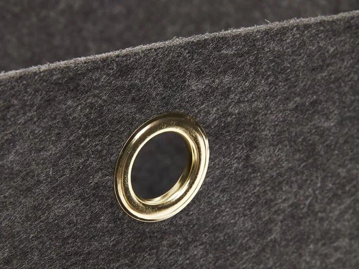 Nærbillede af et gråt filtstof med en guldmetalgennemføring indsat nær kanten, sandsynligvis en del af en organizer eller opbevaringsboks.
