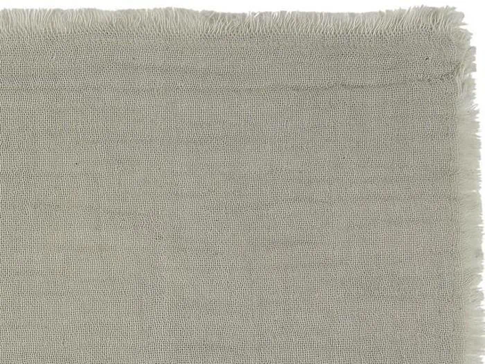 Nærbillede af hjørnet af et lysegråt vævet stof med flossede kanter på toppen og i højre side.