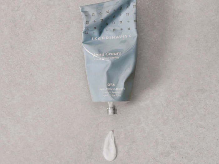 En udpresset tube Skandinavisk håndcreme med en lille mængde hvid creme på en lysegrå overflade.