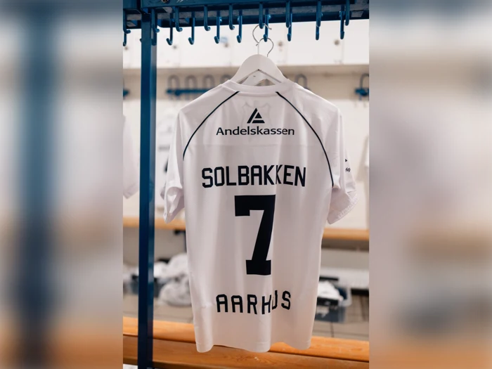 En hvid fodboldtrøje med navnet SOLBAKKEN, nummer 7 og AARHUS trykt på ryggen, der hænger i et omklædningsrum.
