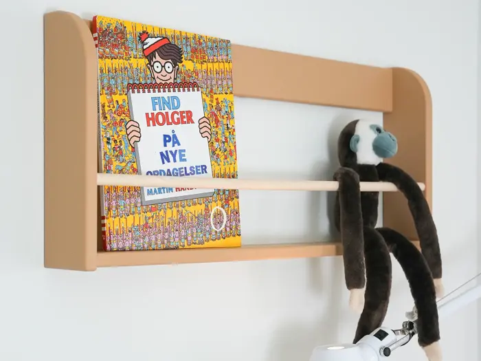 En brun væghængt hylde rummer en Find Holger-bog og en abe i plys, der hænger over den nederste skinne.