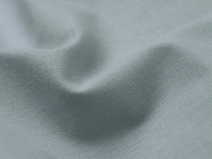 Nærbillede af lyseblåt stof med synlig vævestruktur og blide, bløde folder, der skaber subtile skygger.