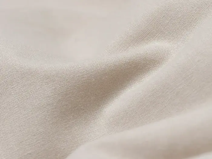 Nærbillede af beige stof med en blød tekstur og blide folder, der fremhæver materialets glatte og let strukturerede overflade.