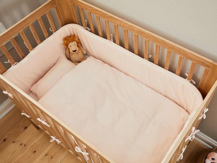 En tremmeseng af træ med lyserødt sengetøj, en pude og en udstoppet løve placeret i det øverste hjørne.