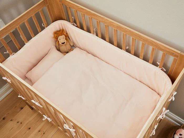 En tremmeseng af træ med lyserødt sengetøj, en pude og en udstoppet løve placeret i det øverste hjørne.