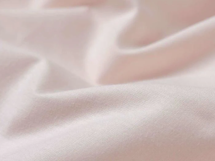 Nærbillede af blødt, lyserødt stof med blide folder og en glat tekstur.
