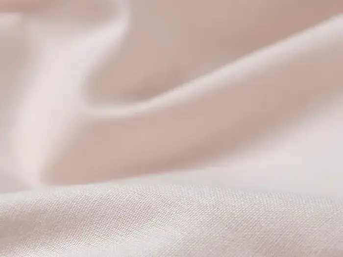 Nærbillede af lyserødt, glat stof med blide folder og blød tekstur.