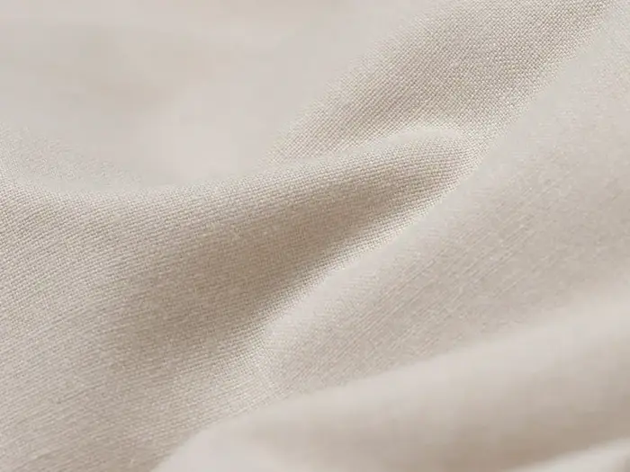 Et nærbillede af glat, cremefarvet stof med blide folder og blød struktur.