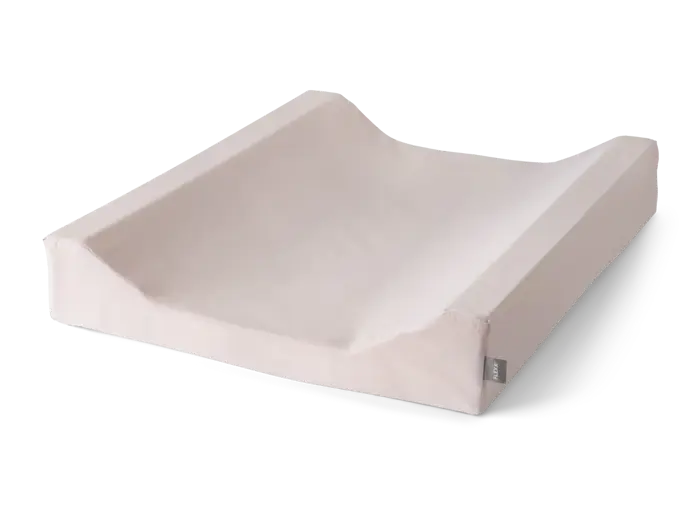 En beige formet puslepude med forhøjede sider og et aftageligt betræk, placeret på en sort overflade.