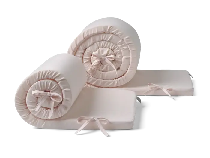 To lyserøde, sammenrullede sengerande med sløjfer, rullet ud i den ene ende, vist på en almindelig baggrund.