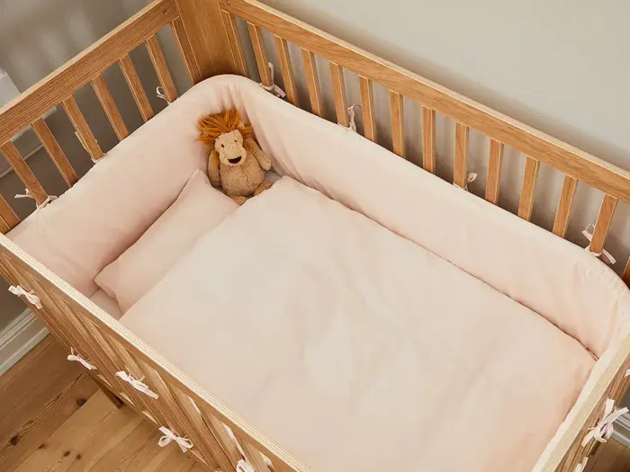 En tremmeseng af træ med lyserødt sengetøj og en løve i plys, der hviler på siden.