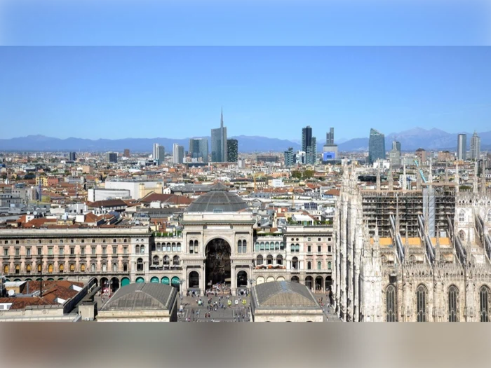 En panoramaudsigt over Milano, der viser Galleria Vittorio Emanuele II, Duomo di Milano og den moderne bys skyline under en klar blå himmel.