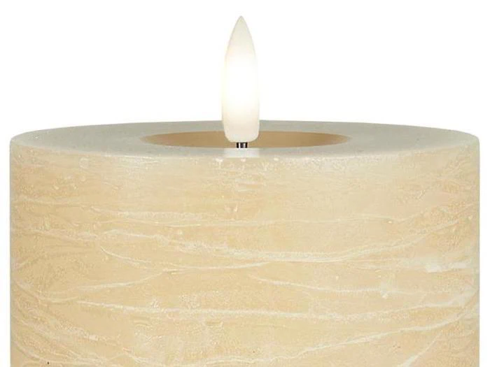 Nærbillede af et beige bloklys med en synlig flamme mod en hvid baggrund.