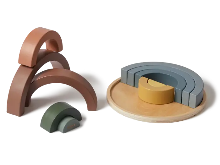 Stabelbart trælegetøj i bløde jordfarver, herunder buede buer og klodser, er anbragt på en rund træbakke og ved siden af den og skaber enkle, minimalistiske strukturer.