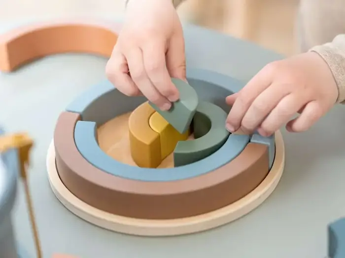 Et barns hænder samler farverige, halvcirkelformede træpuslespilsbrikker på en rund plade.