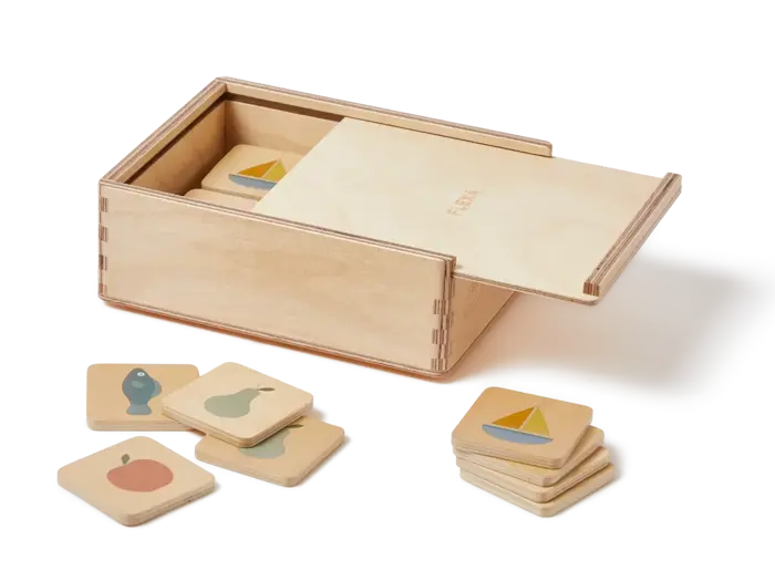 En trææske med skydelåg indeholder kvadratiske brikker med enkle illustrationer af en fisk, en båd, en pære og et æble. Nogle af fliserne er spredt ud ved siden af æsken.