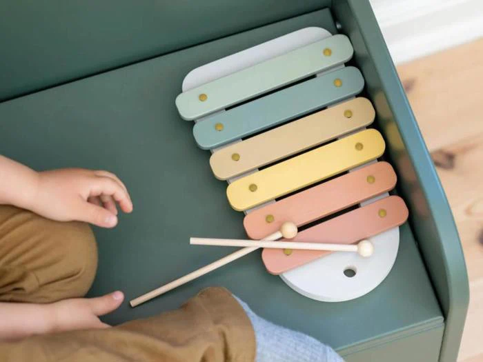 Et barns hænder og ben i nærheden af en pastelfarvet xylofon med to trækøller på toppen.
