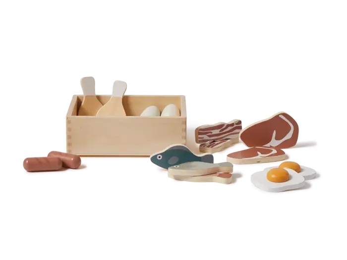Legetøjsmadsæt i træ med en kasse, køkkenredskaber, æg, bacon, bøf, fisk, pølse og et spejlæg, alt sammen arrangeret på en hvid baggrund.