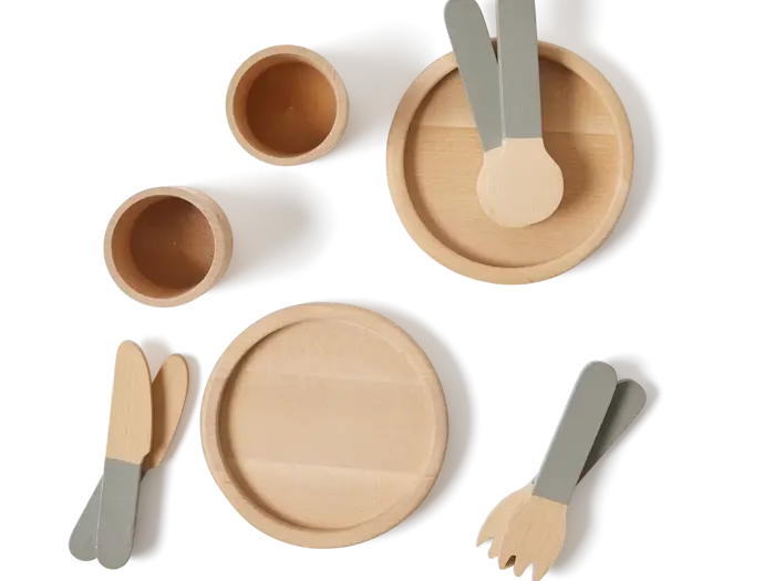 Legetøjssæt i træ med to runde tallerkener, to kopper og seks redskaber (gafler, knive, skeer) med håndtag i naturtræ og grå, arrangeret på en ensfarvet baggrund.
