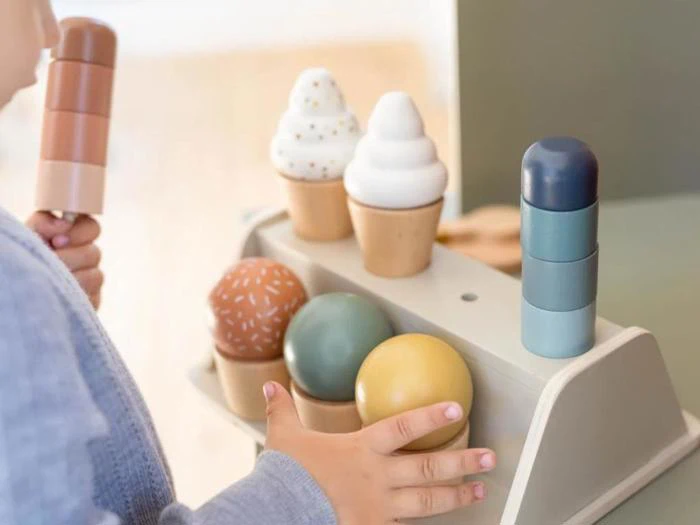 Et barn leger med et legetøjsissæt i træ og holder en vaffel, mens andre legetøjsvafler og -kugler står på et træstativ.