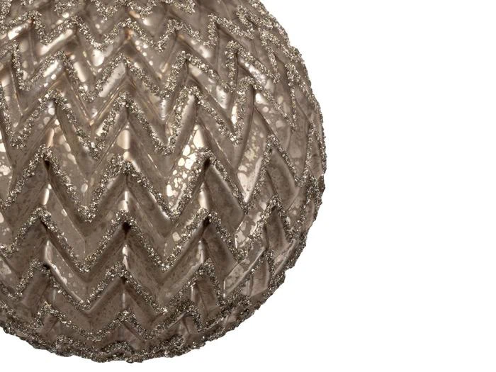 Nærbillede af en rund pyntegenstand med zigzag- og chevronmønster og glitrende detaljer på en hvid baggrund.